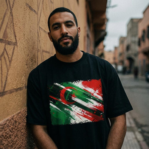 Algeria Les Fennecs Dark. Man wearing a black t-shirt with a colorful graphic design, standing against a wall on a street.