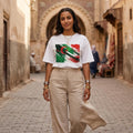 Algeria Les Fennecs Light. Woman wearing a white t-shirt with a green and red design in an alleyway.