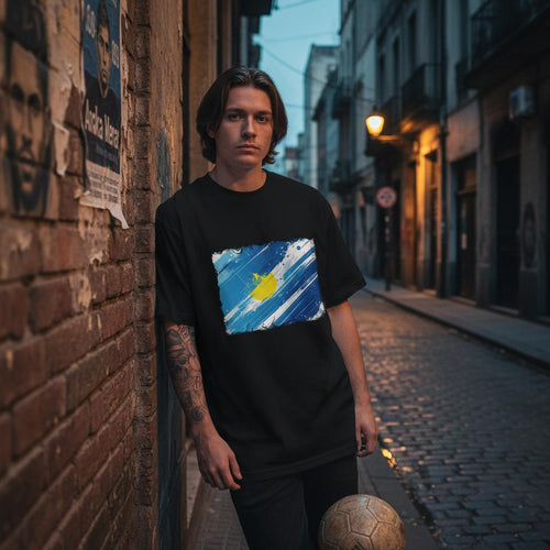 Argentina Albiceleste Dark Mode. Person wearing a black t-shirt with a colorful design, standing on a street.