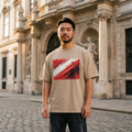 Austria Das Team Sand. Man wearing a beige t-shirt with a red and white design in front of an old building.