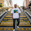 Brazil Selecao Light Mode. Person wearing a white t-shirt with a colorful design on a decorative staircase.