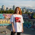 Canada Les Rouges Light. Person wearing a white t-shirt with a red graphic design in an urban setting with graffiti and city skyline.