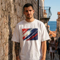 Croatia Vatreni Light. Man wearing a white t-shirt with a red and blue design, standing against a stone wall with a scenic background.
