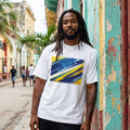 Curacao The Blue Wave Light. Man wearing a white t-shirt with a colorful design, standing in front of a weathered building.