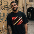 Egypt The Pharaohs Dark. Man wearing a black t-shirt with a red and white graphic design, standing against a textured wall with Arabic text.