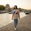 France Les Bleus Sand Mode. Woman walking along a riverside promenade with a scenic cityscape in the background