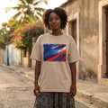 Haiti Les Grenadiers Sand. Woman wearing a beige t-shirt with a colorful abstract design on a street.