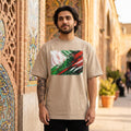 Iran Team Melli Sand. Man wearing a beige t-shirt with a colorful graphic design in front of an ornate building.