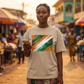 Ivory Coast Les Elephants Sand. Woman wearing a beige t-shirt with a colorful abstract design, standing in a bustling market.