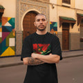 Morocco Atlas Lions Dark. Man wearing a black t-shirt with a colorful design in an urban setting