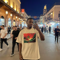 Morocco Atlas Lions Sand. Man taking a selfie in a bustling night market with a colorful flag design on his shirt.