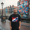 Netherlands Oranje Dark. Man wearing a black t-shirt with a colorful design in front of a graffiti-covered wall.