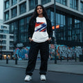 Netherlands Oranje Light. Woman wearing a white t-shirt with a colorful design and black jacket in an urban setting with graffiti.