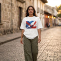 Panama Los Canaleros Light. Woman wearing a white t-shirt with a colorful graphic design on a cobblestone street.