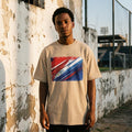 Paraguay La Albirroja Sand Mode. Man wearing a beige t-shirt with a colorful graphic design, standing against a textured wall.