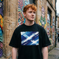Scotland Tartan Army Dark. Person wearing a black t-shirt with a blue graphic design, standing in front of graffiti-covered walls.