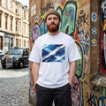 Scotland Tartan Army Light. Man wearing a white t-shirt with a blue graphic design standing in front of a graffiti-covered wall.