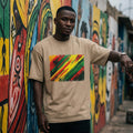 Senegal Lions of Teranga Sand. Man wearing a beige t-shirt with a colorful design in front of a vibrant mural.