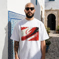 Tunisia Eagles of Carthage Light. Man wearing a white t-shirt with a red and black design, standing in front of a white building with blue accents.