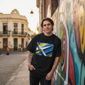 Uruguay La Celeste Dark Mode. Man wearing a black t-shirt with a colorful design, standing in front of a graffiti-covered wall.